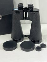 Front view of large black 20x80 binoculars with lens caps and accessories laid out in front, showing textured body and eyepieces.