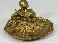 Top view of large brass inkwell with baby figurine in flowing dress forming pen holder base
