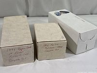 Three owner-labeled white cardboard boxes with hand-written markings indicating the contents: 1991 Upper Deck 1st Edition complete football card set, 1991 Pro Line complete football card set, and a third box with smaller plastic cases and a sealed Super Bowl 25 commemorative card box.