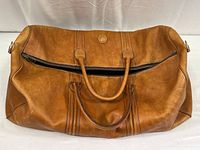 Front view of tan leather satchel with zipper partially open and dual handles visible.