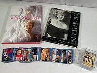 Two Marilyn Monroe coffee table books and a clear plastic box with Marilyn Monroe collectible cards displayed on a white surface.