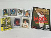 Seven baseball cards plus a Mark McGwire collector's magazine displayed, several cards in clear plastic holders
