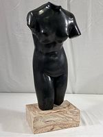 Full view of black basalt female torso sculpture on rectangular beige marble-like pedestal.