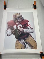 Full view of the Joe Montana poster showing the entire image and white borders, held with clamps at top edges.