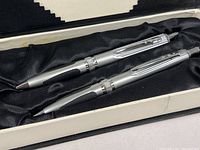 Pen and mechanical pencil lying side by side in original box lined with black satin fabric.