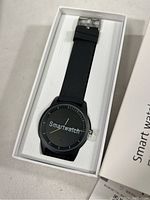 Full boxed black smartwatch with silicone strap placed inside.