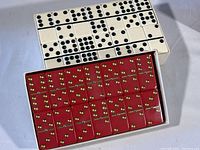 Top view of smaller red domino set pieces sealed in original wrapping inside worn box with gold pips on red tiles.