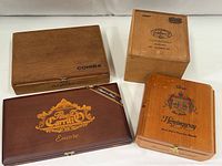 Four vintage wooden cigar boxes displayed from top, showing brand logos and latch details.