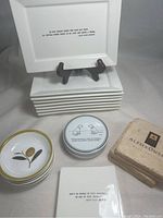 Stack of rectangular white ceramic dishes with printed Ralph Lauren quote, small round dishes with olive design, enclosed coasters box, and small round tin