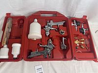 Full view of the open red molded plastic case containing the Husky sprayer kit components including spray guns, fluid containers, and fittings.