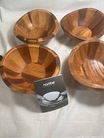 Four Nambe wooden salad serving bowls arranged together with Nambe brochure in front