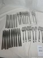 Photo showing 18 forks, 18 knives, and 18 smaller forks or cutting tools, arranged on a white cloth.