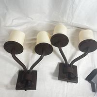 Pair of modern dual-arm wall lamps with frosted white cylindrical shades lying on fabric background, showing overall design and condition