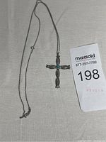 Full view of sterling silver cross pendant with natural turquoise stone and chain against beige background.