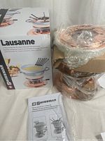 Swissmar Lausanne fondue set box with components partially unpacked, showing copper and stainless steel elements and instructions.