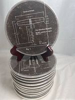 Stack of 12 round appetizer dishes with printed corkscrew technical drawing design, labeled Tire Bouchon 2911, showing measurements and parts in French.