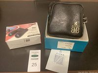 Birks carrying case with birks box and Konus boxed binoculars on a table with a numbered tag and a Birks brochure.