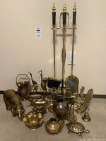 Full view of brass fireplace tools with black marble handles and base, surrounded by various brass decorative figurines including dolphins, birds, turtle, elephant, and candlesticks.