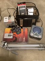 Camera and camcorder lot laid out on floor including Vivitar tripod, Pentax Espio 60 camera box, Canon camera case, digital timer, RCA CD alarm clock, Elura camcorder, Sony DVC camcorder and more