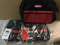 Craftsman black tool bag with front mesh pocket and red accent placed next to two Jobmate tool bags in packaging.