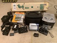 Full lot including tripod, box, battery chargers, Kodak charger in packaging, camera bag, RCA clock radio, Canon camcorder and digital cameras, assorted batteries