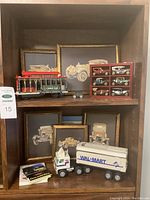 Wide view of shelf showing Walmart truck radio, framed antique car prints, miniature antique model cars in wooden display case, and additional items.