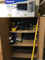 Wide shot of wooden cabinet containing various painting supplies including extension poles, paint rollers, paint chip books, spray bottles, and storage boxes.