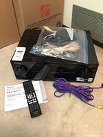 Photo showing the front and top of the black Pioneer VSX-821 receiver alongside remote control, manual, and multiple cables in a plastic bag and loose purple speaker wire.