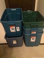 Five Rubbermaid storage bins stacked, showing colors and general condition with some marks on the lids.