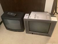 Two CRT televisions side by side, one black Sharp unit and one grey Toshiba unit with remote placed on top of black TV