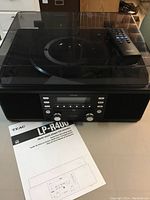 Full front view of Teac LP-R400 multi music player showing turntable with closed dust cover, front panel with controls, remote on top, and instruction manual on table.