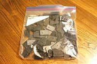 Photo showing a large collection of about 120 black plastic rectangular display stands in a clear ziplock bag on a wooden surface.