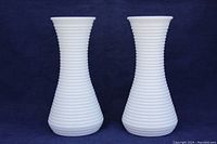 Two identical opaque white milk glass vases with horizontal ribbing standing side by side against a dark background.