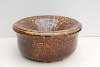 Front angled view of brown glazed antique pottery spittoon with wide flared rim and mottled glaze.