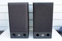 Front view of pair of black Monitor Audio Bronze2 bookshelf speakers with grills on showing bass ports and logo on front.