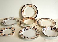 Full lot showing seven pieces of English dishware with floral and gilt pattern on white base.