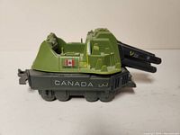 Side view of G.I. Joe Slam Tank toy vehicle showing Canadian flag and CANADA label on dark gray base with green upper tank structure.