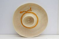 Top down view showing the bowl shape and central dip area, textured ceramic resembling weave pattern, cream colored with an orange band around raised central cup.