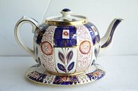 Side view of the ceramic teapot on its ceramic matching trivet showing the floral and geometric design in Imari colors