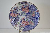 Front view of a round vintage Japanese porcelain charger plate decorated with pink, blue, and green floral and blue geometric patterns.