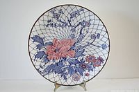 Front view of the round porcelain charger plate showing intricate floral design with pink and blue flowers and lattice background.
