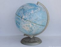 Full view of the vintage Rand McNally world globe on its metal spinning base showing the globe's surface, topography, and color scheme.