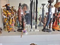 Photo showing multiple African figurines, including cloth dolls and wooden statues arranged on a shelf.