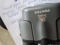 Close-up of the Pentax 9x21 mini binoculars top side with brand and specifications visible.