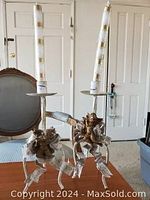 Pair of metal candle holders each holding a tall white candle with beige stripes, featuring decorative bows on the holders.