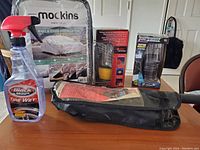 Photo showing all items: Moc-Kins small car cover in packaging, Black Magic Tire Wet tire cleaner spray bottle (half full), black zippered car duster bag, yellow LED lantern in box, and a silver/black LED lantern in packaging.