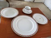 Four pieces laid out on table: soup bowl, cup with saucer, salad plate, bread and butter plate, showing the red, green, white geometric pattern with gold trim on white china.
