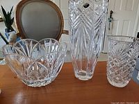 Photo showing three clear cut crystal items on a wooden table: tall vase, medium vase, and large bowl.
