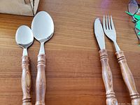 Wooden handled cutlery spoon, fork and knife with tiki pattern carved handles on wooden surface.