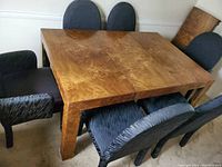 Rectangular burl wood dining table with six upholstered chairs around it, extension leaf leaned against the wall